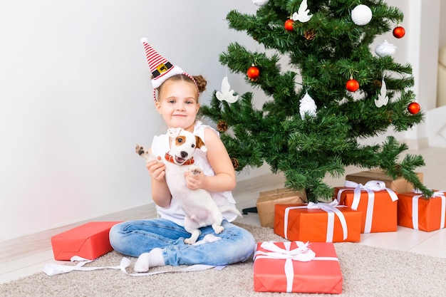 Christmas, pets and holidays concept - Child in santa hat with a jack russell terrier puppy.