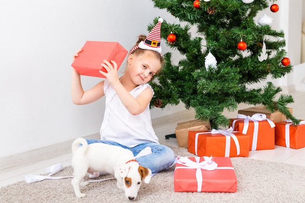 Christmas, pets and holidays concept - Child in santa hat with a jack russell terrier puppy.