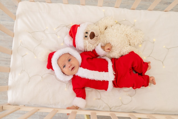 Christmas photo of a baby in a Santa costume lying in a crib at home