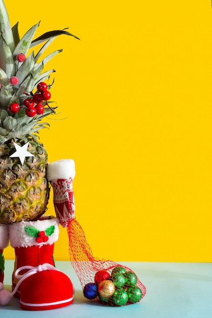 Ananas natalizio in stivali da babbo natale, muffole invernali e un sacchetto di caramelle color cioccolato