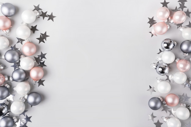 Фото Рождественские розовые и серебряные безделушки, звезды конфетти как рамка на пастельных сером фоне. вид сверху с пространством для текста. квартира лежала.