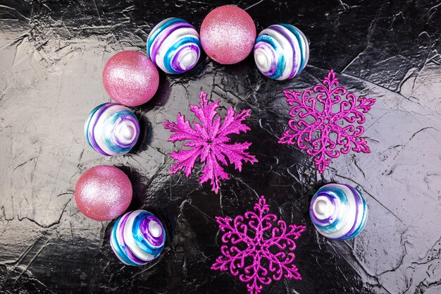 Christmas pink and purple balls and decorative snowflakes on black background.