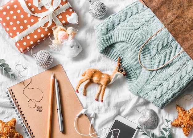 Christmas planning and shopping background blue knitted sweater\
in a paper bag notepad phone christmas decoration on a light\
background top view christmas still life