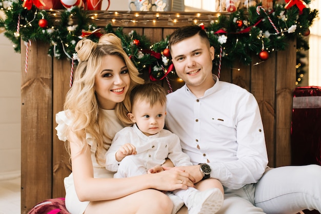 Фото Рождественский портрет молодых родителей с маленьким сыном с рождественский бар. новый год и рождество концепция