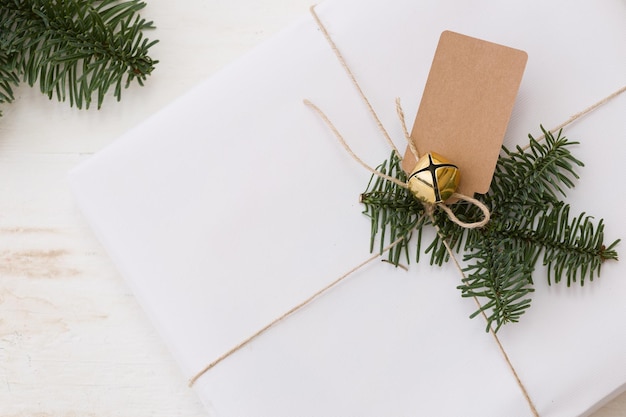 Christmas present in white box with fir branches and tag at white wooden table