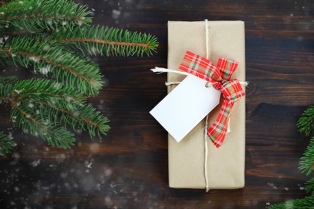 Christmas present with white label on wooden background with fir branch on one side