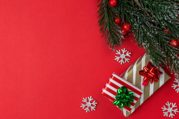 クリスマス プレゼントとクリスマス ツリーの枝とヒイラギ トップ ビュー コピー スペースと赤の背景に赤と金色の縞模様の紙のギフト