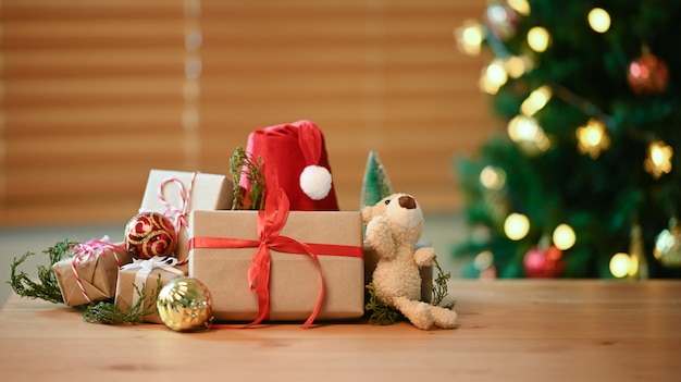 Рождественские подарки, шляпа Санты и плюшевый мишка на деревянном столе в гостиной.