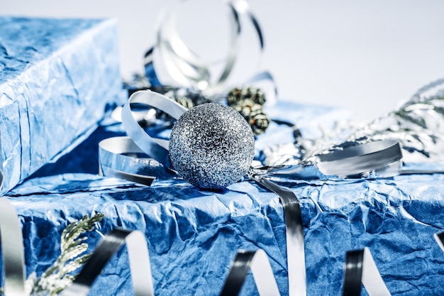 Фото Рождественские подарки с подарочной коробке в серебристо-синем цвете, украшенной сосновыми шишками и ветками на белом фоне, подготовка к праздникам. рождественские подарки и новый год. ручной работы. выборочный фокус.