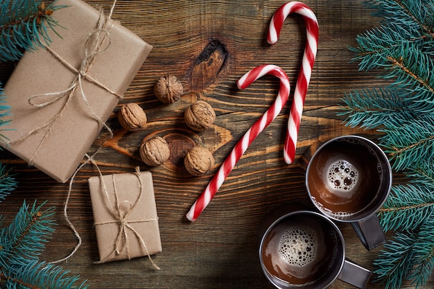 Photo christmas presents with two cups of cappuccino nuts cones and fir branch on wooden background close up