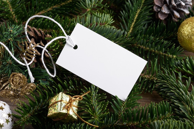 Christmas rectangle white tag mockup with white cord close up on natural fir tree branch with Christmas decoration