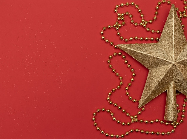 Christmas red background with golden star - the top of Christmas tree and golden beads.