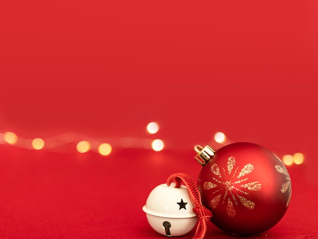 Photo christmas red bauble with a white jingle bell design in a red background with yellow lights bokeh