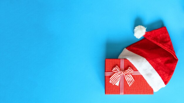 Christmas red gift decorated with red ribbon in santa claus hat isolated on blue background, close up, flat lay, copy space