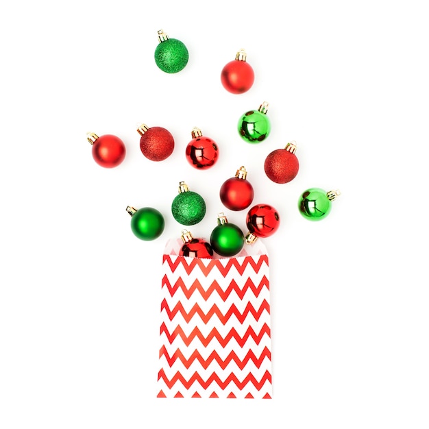 Christmas red and green balls  flowing from a gift bag on white background Flat lay, top view trendy holiday concept.