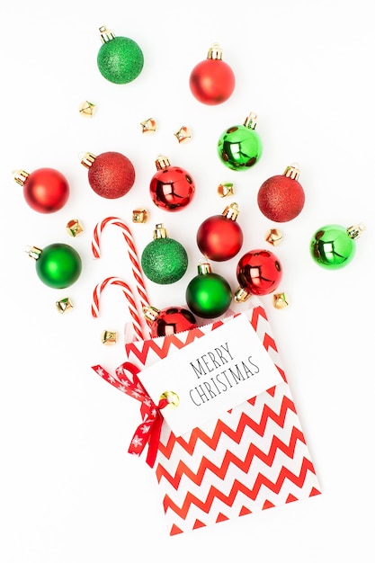 白い背景の上のギフトバッグから流れるクリスマスの赤と緑のボールフラットレイ、トップビュートレンディな休日のコンセプト。