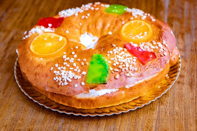 Christmas round fruit cake decorated with fir tree branch, glazed fruits and nuts on a wooden table.