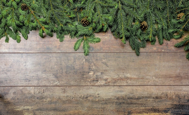 クリスマスの素朴な背景クリスマスの冬の休日の挨拶のテンプレートコピースペースのある暗い木製のテーブルの上のクリスマスツリーの枝と円錐形クリスマスモミの枝のある暗い素朴な木製のテーブル