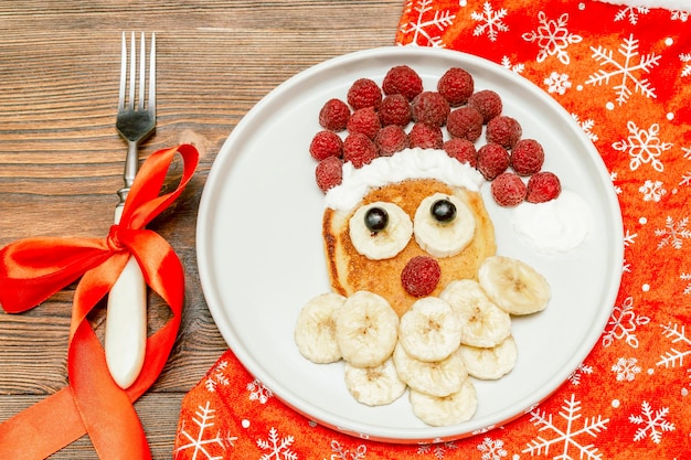 사진 크리스마스 산타클로스 모양의 팬케이크 신선한 라즈베리 베리 바나나 어린이 어린이 아침 식사 크리스마스 음식 나무 배경에 새해 장식