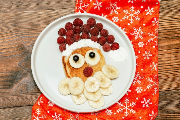 Christmas Santa Claus shaped pancake with sweet fresh raspberry berry and banana on plate on wooden