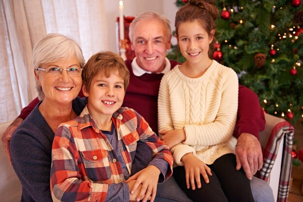Christmas senior couple and couch with grandchildren happiness and relax for festive season at home Xmas love and elderly man with mature woman grandkids or happy with smile content or portrait