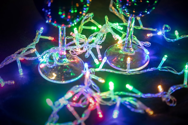 Christmas shining multicolored garland reflected in glass glasses on a dark background. New Year celebration....