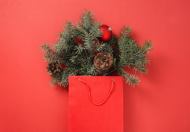 Christmas shopping concept Paper bag full of fir tree and christmas balls with pine cone on red  top view