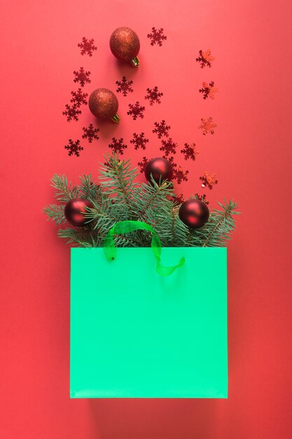 Christmas shopping green paper bag with red baubles and shiny snowflakes on red space