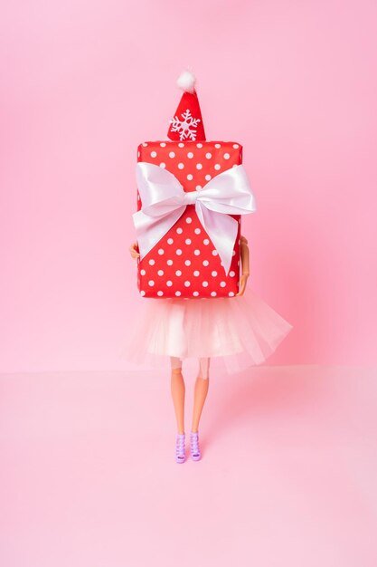 Christmas shopping minimal concept A doll with Xmas present in her hands on pink background