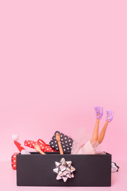 Christmas shopping minimal concept Santa's hat legs and arms of the doll are visible from the Christmas present on a pink background