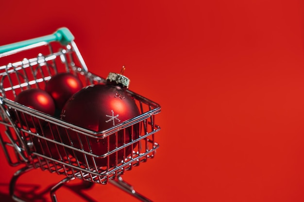 Рождественская тележка для покупок с красными рождественскими украшениями шарами на красном фоне минимальное рождество
