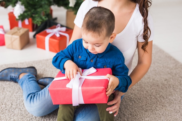 クリスマス、ひとり親、休日のコンセプト-家で母親へのクリスマスプレゼントを持っているかわいい男の子。