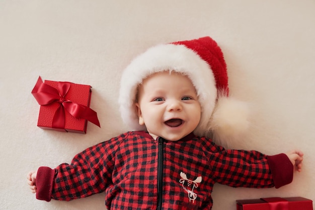 Foto neonato sorridente di natale in cappello della santa con i regali.