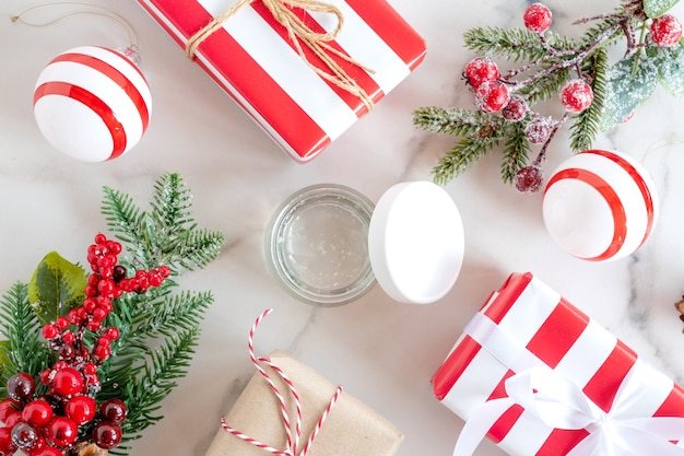 Christmas Spa Concept and Winter Skin Care products, fir branches and gift boxes on marble background, flat lay, copy space. Seasonal beauty routine and skin care concept.