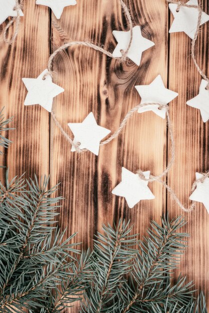 Christmas stars homemade cold porcelain garland with spruce branches on background of burnt wood, top view. Vertical