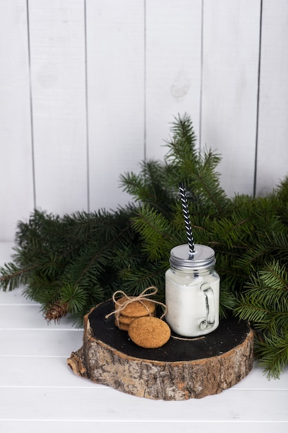 Christmas still life scene. Scented candle in a glass jar and cookies on a thick wooden log near a spruce branch