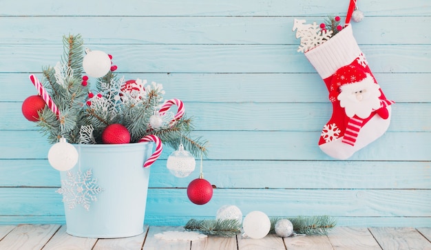 Christmas stocking and fir branches in blue bucket on blue wooden background