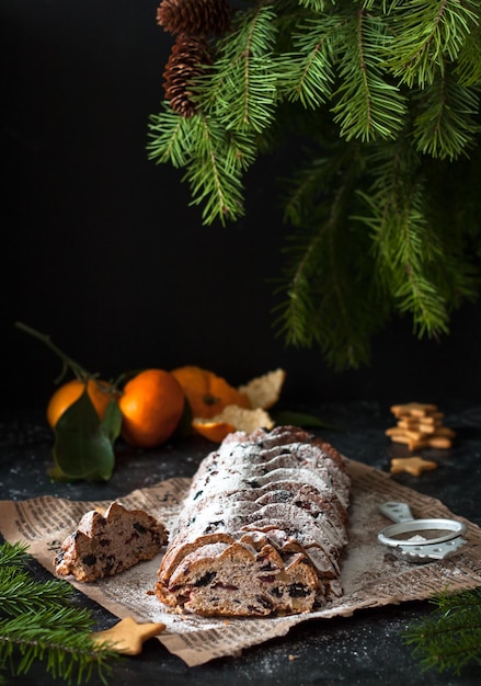 Foto stollen di natale su uno sfondo scuro dolce natalizio tradizionale tedesco tagliato a pezzi torta con noci uvetta marzapane e frutta secca su un giornale cottura per natale