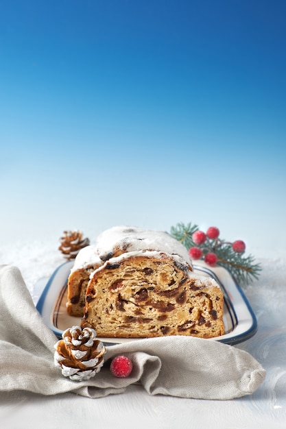 Natale stollen sulla superficie festiva bianco-blu con ramoscelli di abete e bacche, spazio del testo