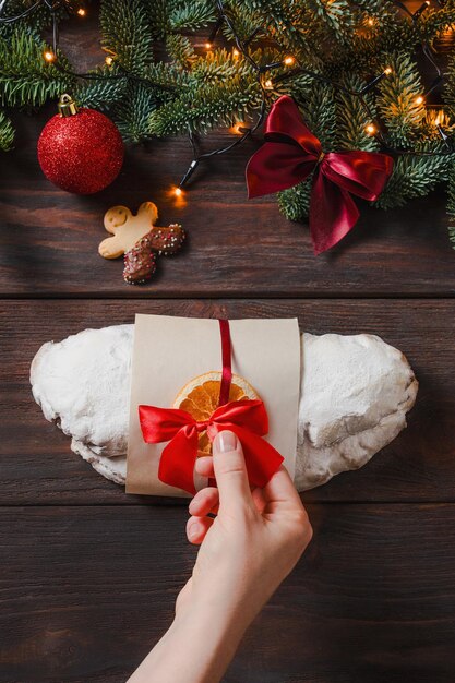 Christmas stollen with marzipan and dried fruits on dark background Festive Christmas light holiday mood cheerful time Female hands decorate stollen for market