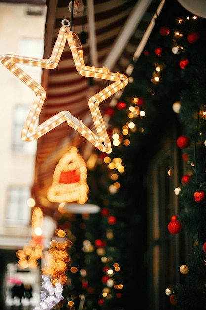 Christmas street decor Stylish christmas golden star illumination and fir branches with red and gold baubles golden lights bokeh on front of building at holiday market in city street