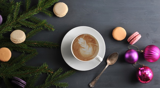 Christmas surface with Cup of cappuccino with cake, macarons, Christmas toys and tree branches