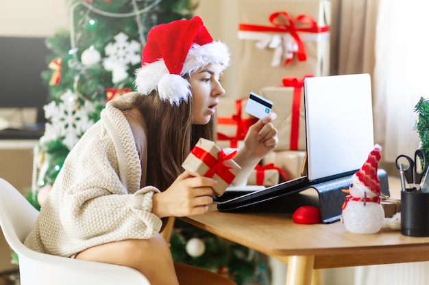 プレゼントボックスとクリスマスの周りにインターネットショッピングをしているラップトップを探しているクリスマスの驚きの女性