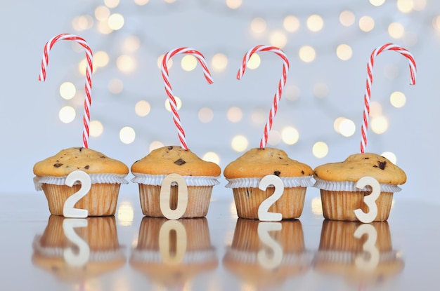 Christmas sweet cupcakes and candles in form of numbers 2023. White background with bokeh. New year