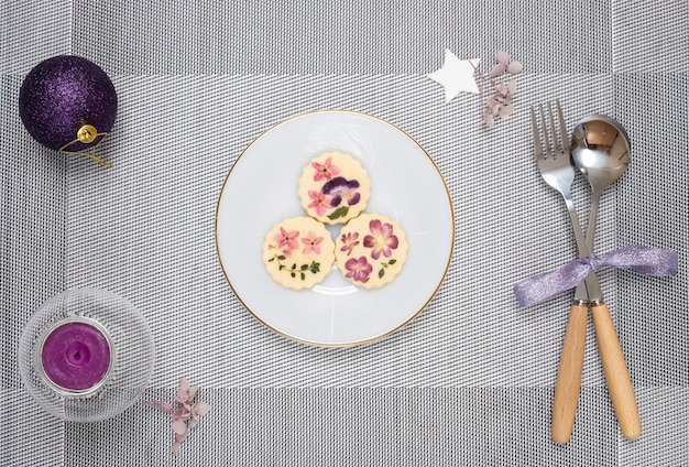 Christmas table decorations with a plate of edible flower biscuits and scented candle