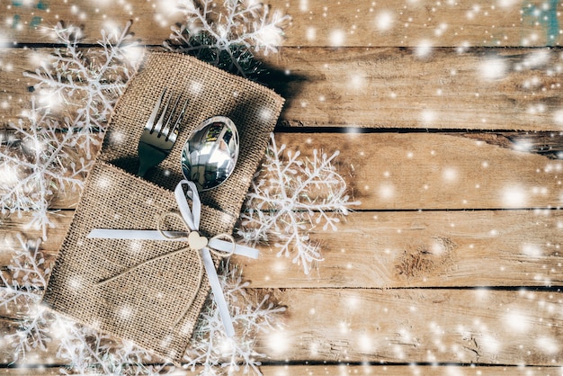 christmas table place setting and silverware, snowflakes with snow winter on table wooden background