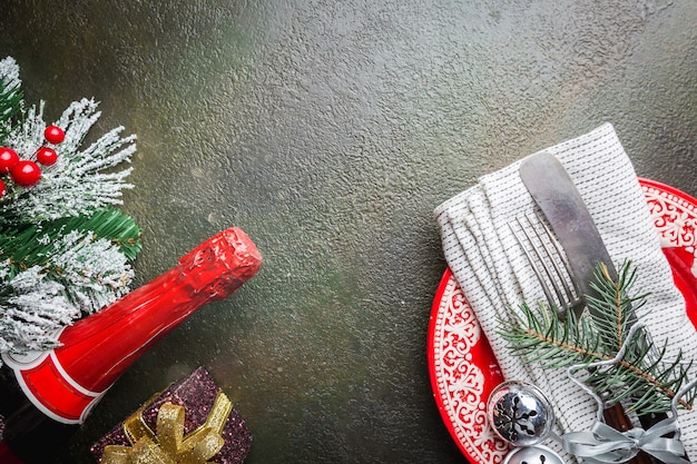 Christmas table place setting with christmas tree branches, champagne, plate, knife and fork over dark table, top view with copyspace. Christmas holidays background