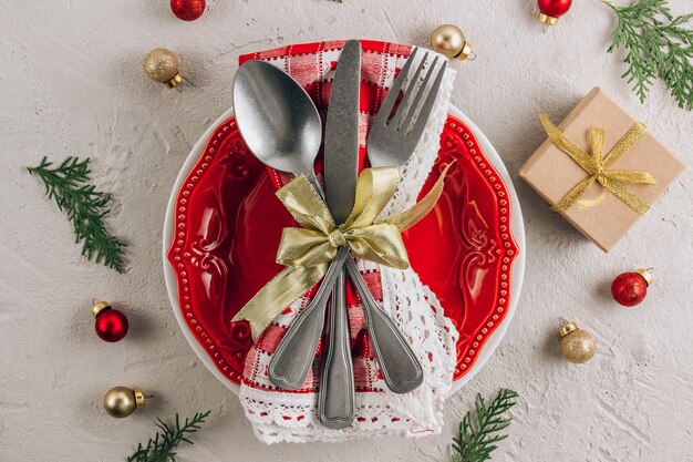 Christmas table place setting with empty red plate, cutlery on napkin