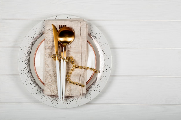 Photo christmas table setting concept on white wooden background. plate, napkin and golden cutlery and christmas decorations on white background top view, free space for text. high quality photo