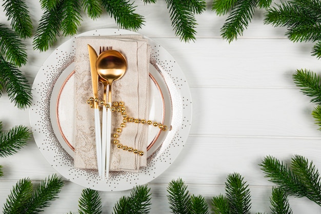 Christmas table setting concept on white wooden background plate napkin and golden cutlery and